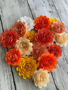 paper flowers arranged in the shape of a heart on a wooden table with white boards