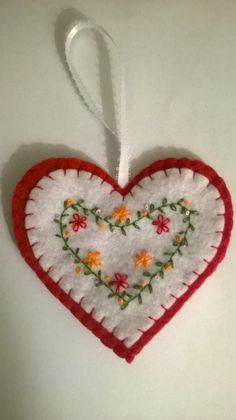 a red and white heart ornament with flowers on it's side hanging from a string