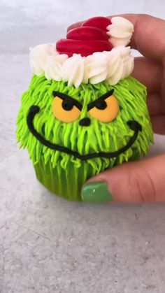 a hand holding a cupcake with green frosting and a grin face on it