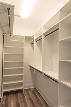 an empty walk in closet with white shelving and wood flooring on the side