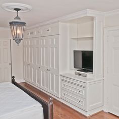 an empty bedroom with white furniture and a large tv on the dressers next to the bed