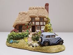 a toy car is parked in front of a house with a thatched roof and flowers