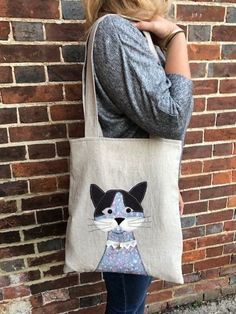 a woman standing next to a brick wall holding a bag with a cat on it