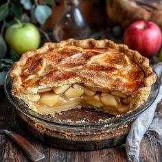 an apple pie on a wooden table with apples in the background