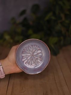 a person's hand holding a small plate with a flower design on the side