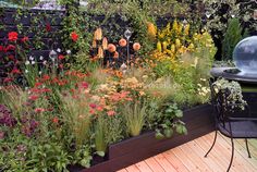 a garden filled with lots of different types of flowers and plants next to a grill