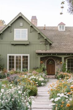 a green house with lots of flowers in the front yard and walkway leading to it