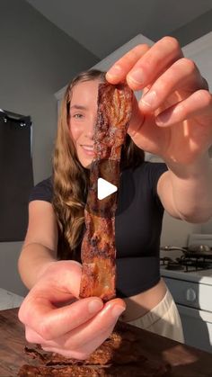 a woman holding up a piece of bacon in her hands