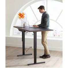 a man standing at a desk using a laptop computer with an orange lamp in the background