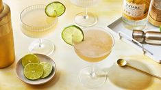 three glasses filled with different types of alcohol and limes on a table next to bottles