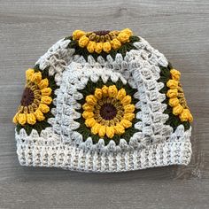 a crocheted hat with sunflowers on the front and bottom, sitting on a wooden surface