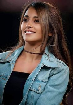 a woman with long hair wearing a blue jacket and black top smiling at the camera