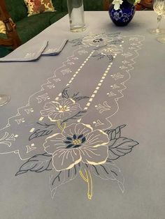 an embroidered table runner with flowers on it and place settings to the side, along with wine glasses