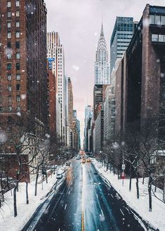 a city street with snow falling on the ground and tall buildings in the backgroud