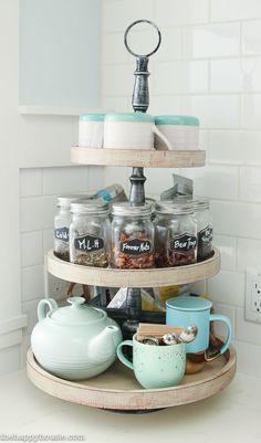 three tiered spice rack in the corner of a kitchen with jars and mugs on it