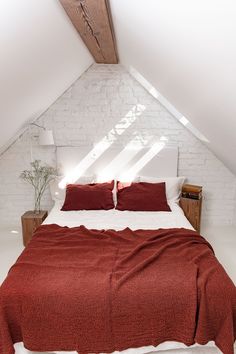 a bed with red blankets and pillows in a loft space under a slanted ceiling