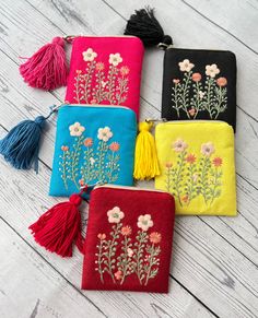 four small embroidered pouches with tassels and flowers on them sitting on a wooden surface