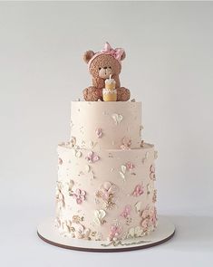 a three tiered cake with a teddy bear on top and flowers all over it