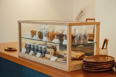 a display case filled with lots of food on top of a wooden counter next to plates and bowls