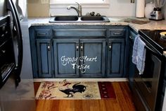 a kitchen with blue cabinets and wood flooring in the middle, along with a rug on the floor