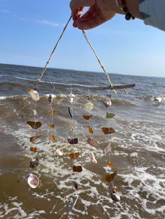 a person is holding up a wind chime on the beach near the water's edge