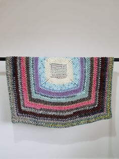 a multicolored crocheted rug hanging on a clothes line with a white wall in the background