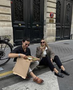 a man and woman sitting on the sidewalk next to a box of pizza with toppings