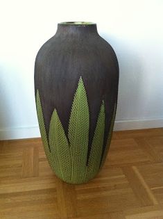 a large vase sitting on top of a hard wood floor next to a white wall