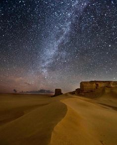 the night sky is filled with stars above sand dunes and rock formations in the desert