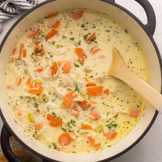 a pot filled with chicken and carrots on top of a table next to a wooden spoon