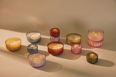 many different colored candles sitting next to each other on a white surface with shadows coming from them