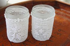 two white glass jars sitting on top of a wooden table next to a coffee cup