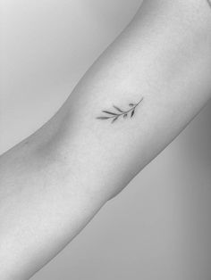 a black and white photo of a person's arm with a small branch tattoo on it