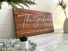 a wooden sign that says the wedding on it next to potted plants and greenery