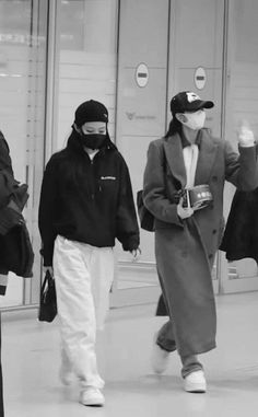 three people walking down the street in winter clothes, one wearing a face mask and holding a cell phone