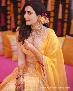 a woman in yellow dress sitting down with her hands on her chest and wearing jewelry