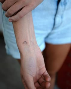 a person with a small wrist tattoo on their left arm, holding the other hand