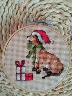 a cross - stitch christmas ornament with a dog and presents on it's side