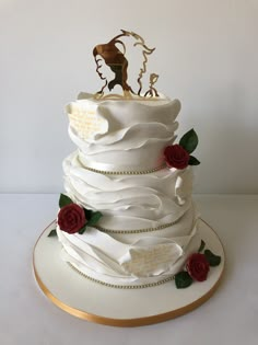 a white wedding cake with red roses on the side and a gold plated decoration