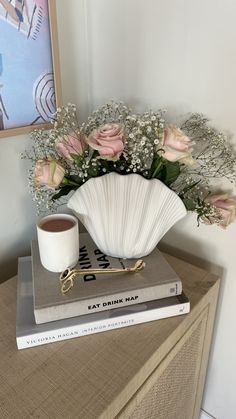 a vase filled with flowers sitting on top of a stack of books next to a cup