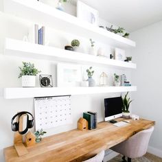 a wooden desk topped with a computer monitor next to a wall mounted shelf filled with potted plants