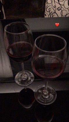 two wine glasses sitting next to each other on top of a table with a red heart in the middle