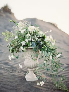 a vase filled with flowers sitting on top of a sandy beach next to a hill