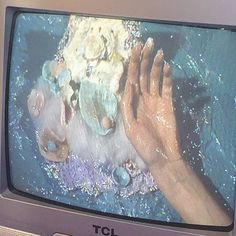 an old tv with someone's hand on it and other items in the water