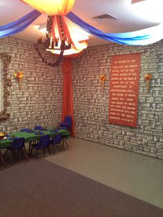 an empty room with tables and chairs in front of a brick wall that has blue drapes hanging from the ceiling