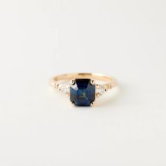 a gold ring with a blue sapphire and three diamonds on the side, sitting on a white surface