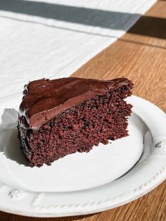 a piece of chocolate cake on a white plate with a wooden table in the background