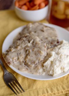 a white plate topped with mashed potatoes and gravy next to a bowl of carrots