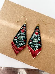 a pair of beaded earrings sitting on top of a piece of paper next to a ruler