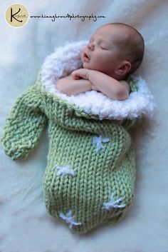 a baby wrapped in a green knitted sweater sleeping on top of a white blanket